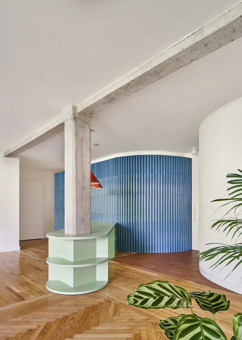 Curved pale green planter wrapping around an exposed concrete column with herringbone wood flooring
