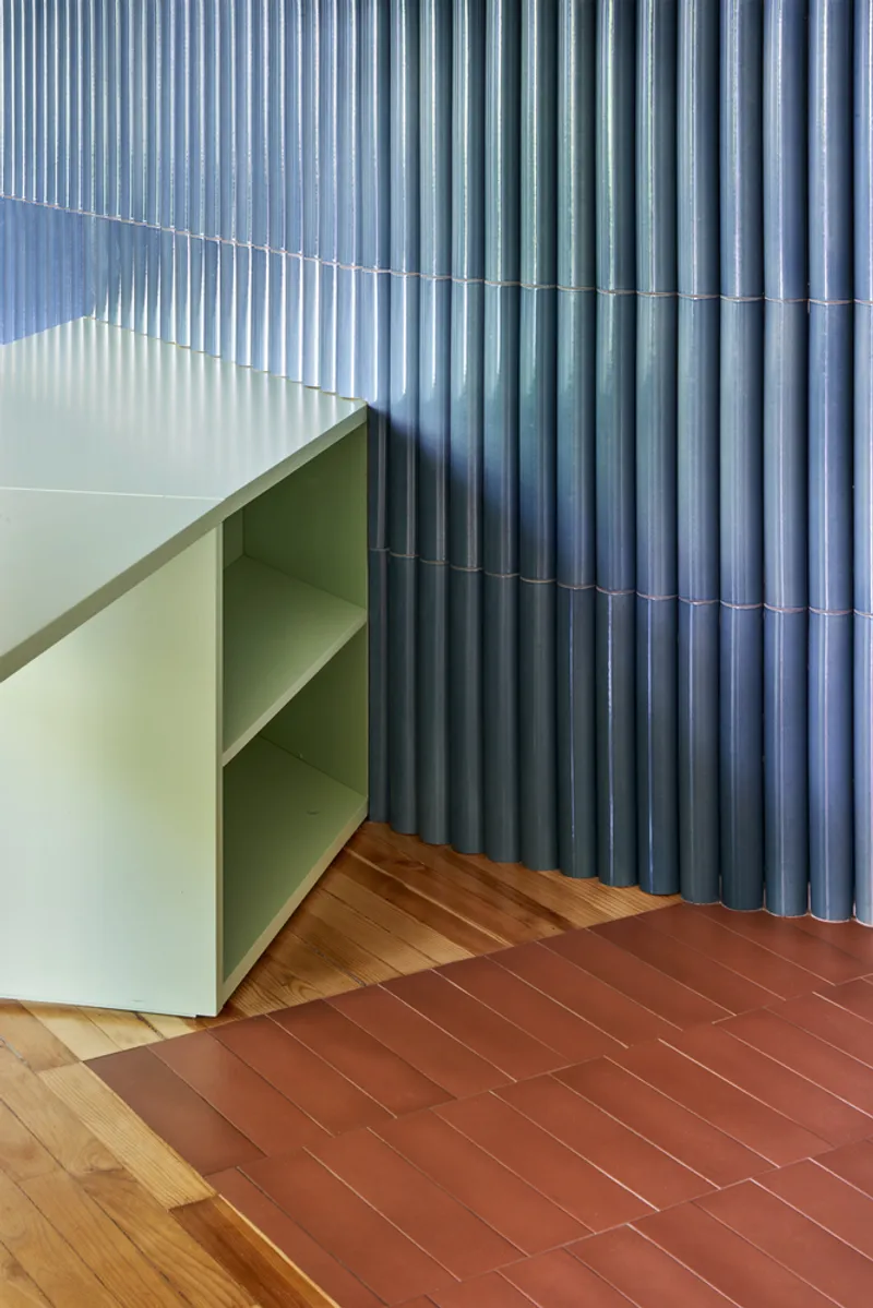 Detail of pale green curved cabinet edge against blue corrugated wall with terracotta floor tiles