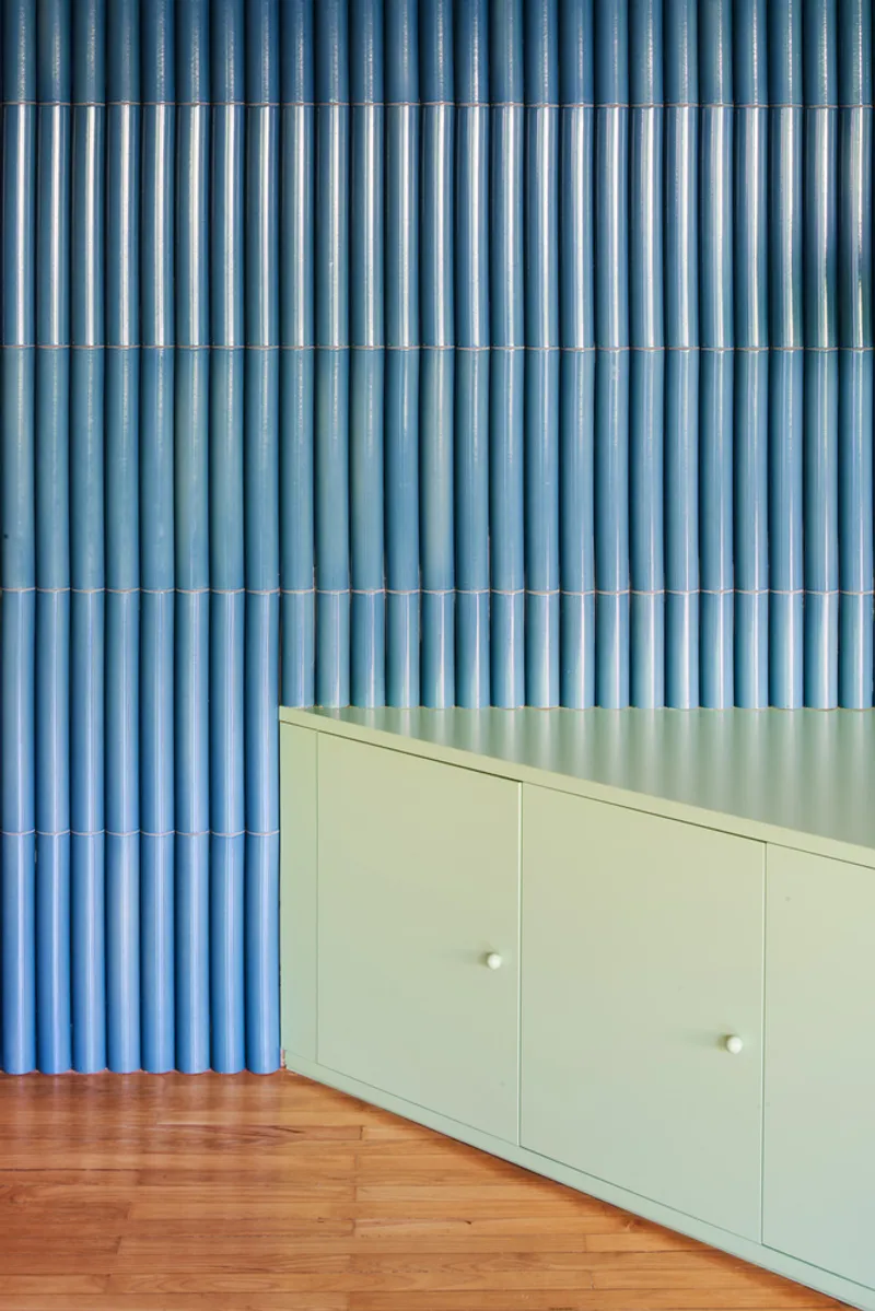 Blue corrugated wall behind pale green cabinet on wood floor with terracotta tile detail