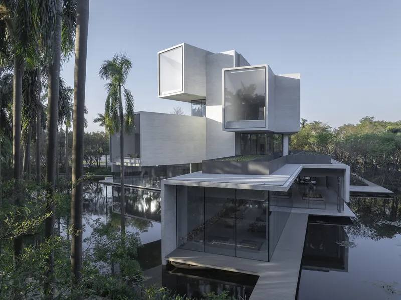 Stacked white concrete volumes reflected in a still pond surrounded by palm trees