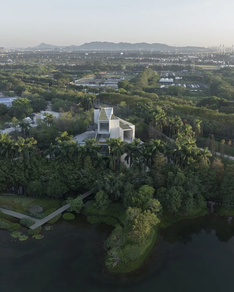 White geometric volumes elevated above palm trees with distant hills visible under hazy sky