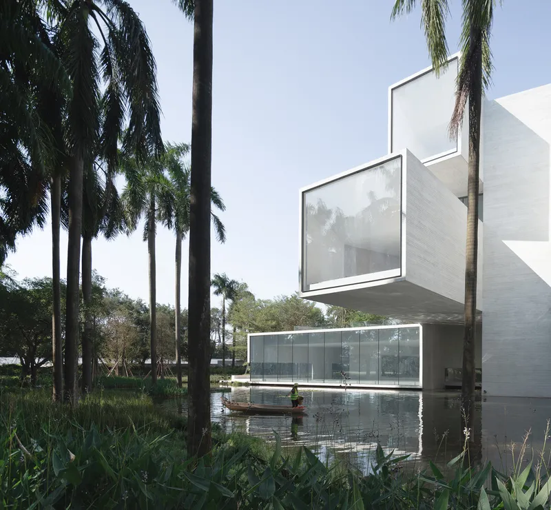 Cantilevered glass-enclosed volumes reflected in the adjacent pond beneath tall palms
