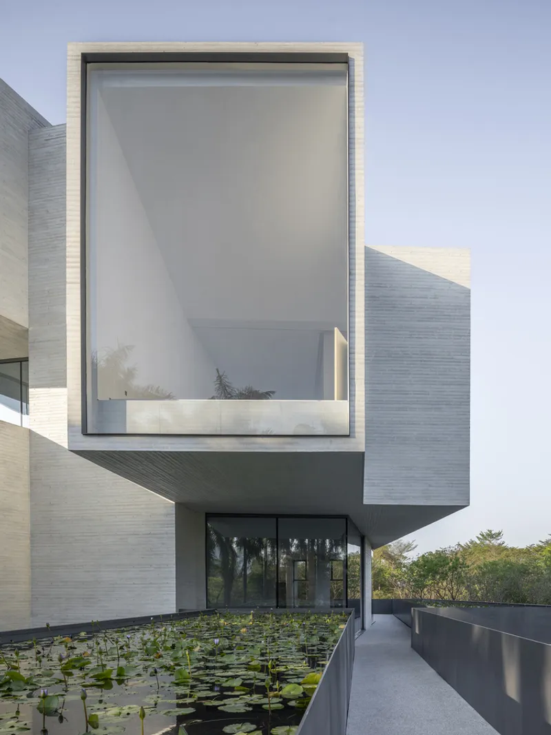 Cantilevered glass-walled volume overlooking a lily pond along a concrete walkway at dusk