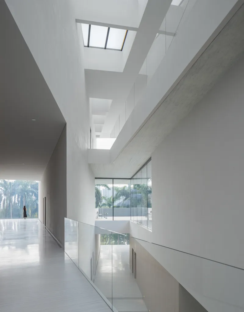 Double-height gallery with glass balustrade and skylights above ribbed concrete walls
