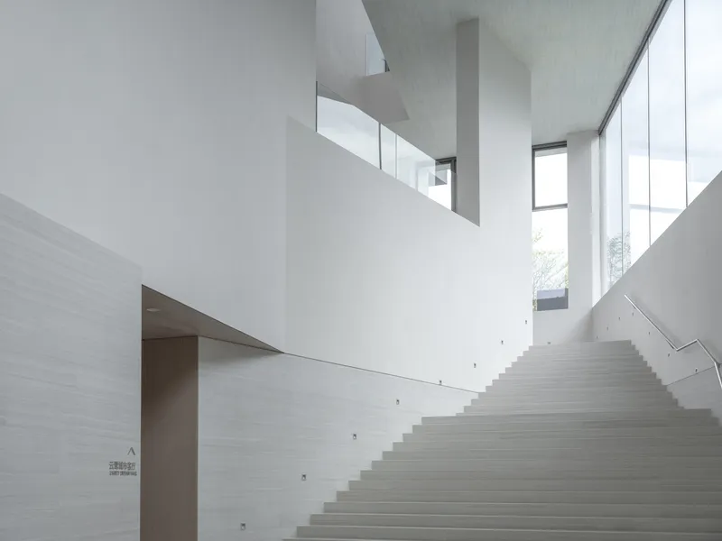 Concrete staircase ascending toward clerestory windows in a white-walled atrium