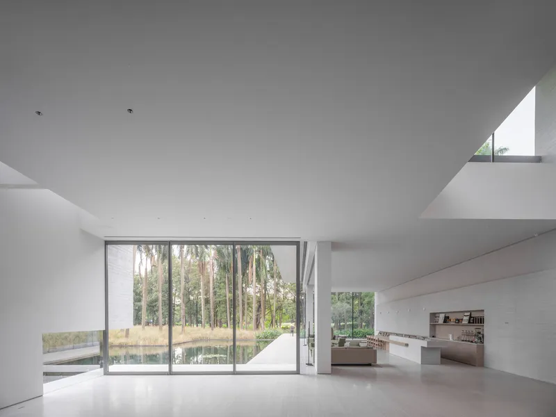Double-height living space with full-height glazing opening onto a pond and grove of tall trees