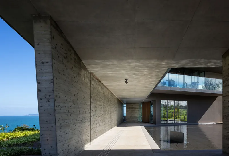 Covered entrance passage with board-formed concrete walls and reflecting pool under clear blue sky