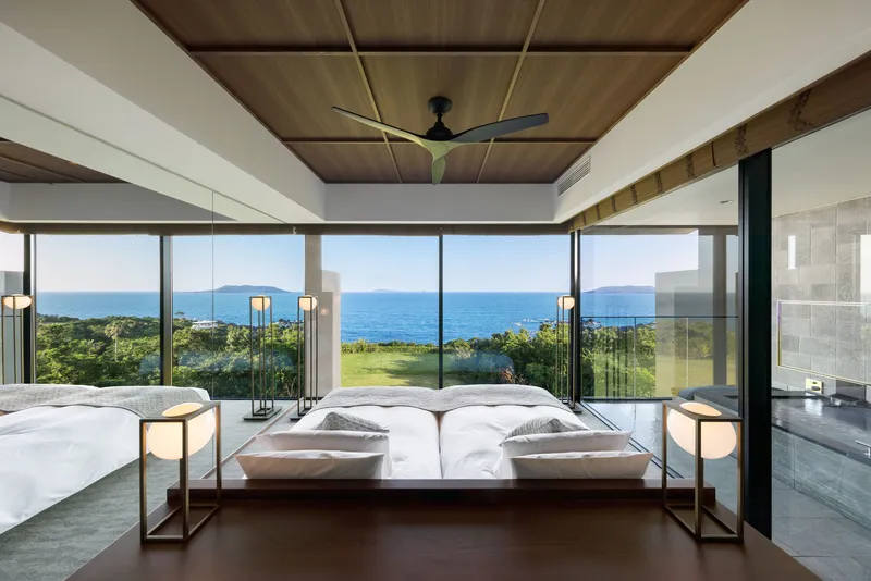 Bedroom with floor-to-ceiling glass walls opening to ocean views and coastal vegetation beyond