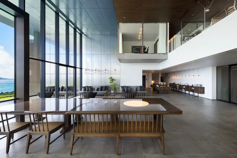 Double-height dining and living space with suspended mezzanine and floor-to-ceiling glazing facing the ocean