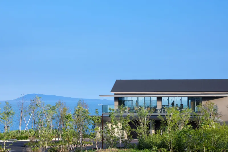 Exterior view of glazed upper level above landscaped terrace with young trees and distant mountains