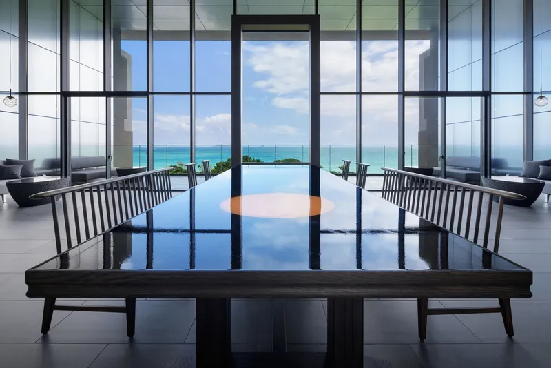 Lobby seating with black lacquered table and floor-to-ceiling glazing framing turquoise ocean views