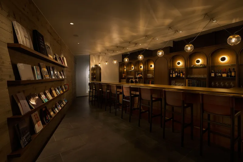 Bar interior with arched shelving niches, pendant globe lights, and timber display wall under low warm lighting