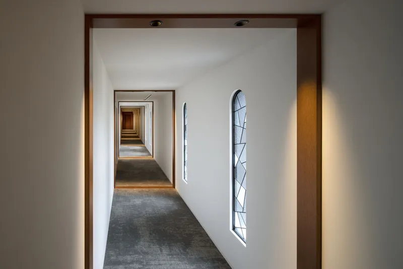 Corridor with timber-framed doorways receding in perspective and vertical leaded glass windows along white walls