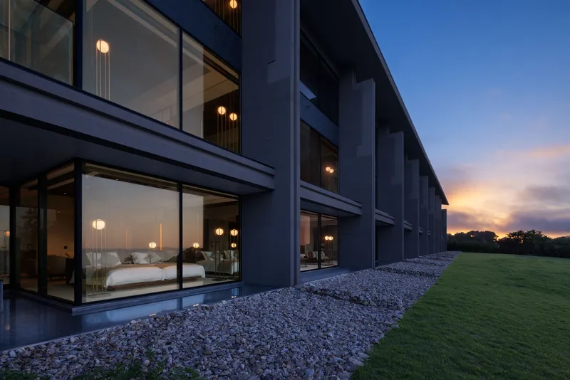 Two-storey glazed facade with white stone gravel bed and illuminated interiors at dusk