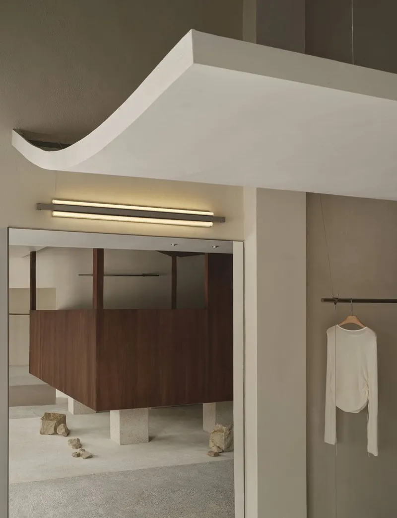 Detail of curved ceiling edge with linear light fixture above framed opening and hanging white garment