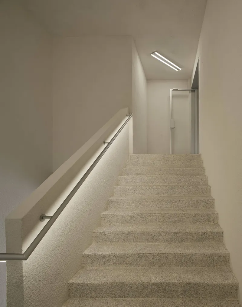 Terrazzo staircase ascending toward skylight with metal handrail and recessed linear illumination
