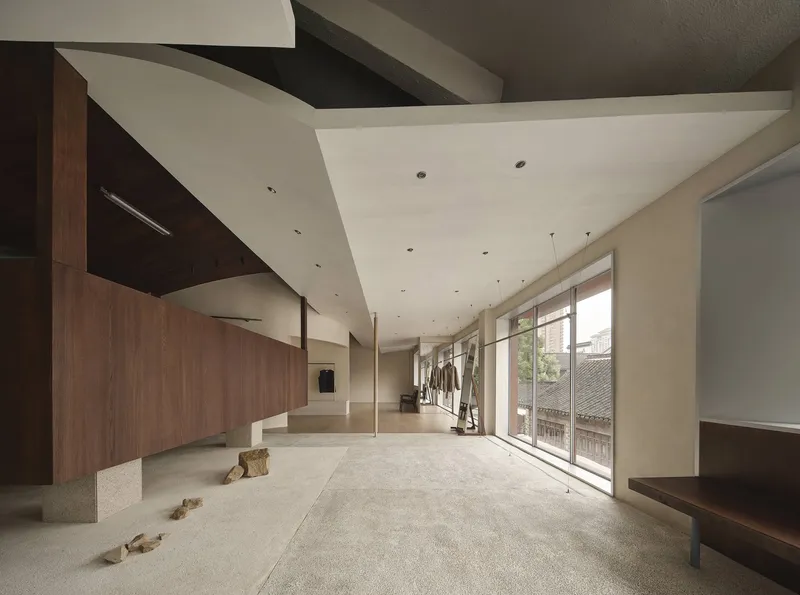 Double-height interior space with folded plaster ceiling, timber walls and scattered rocks on terrazzo flooring