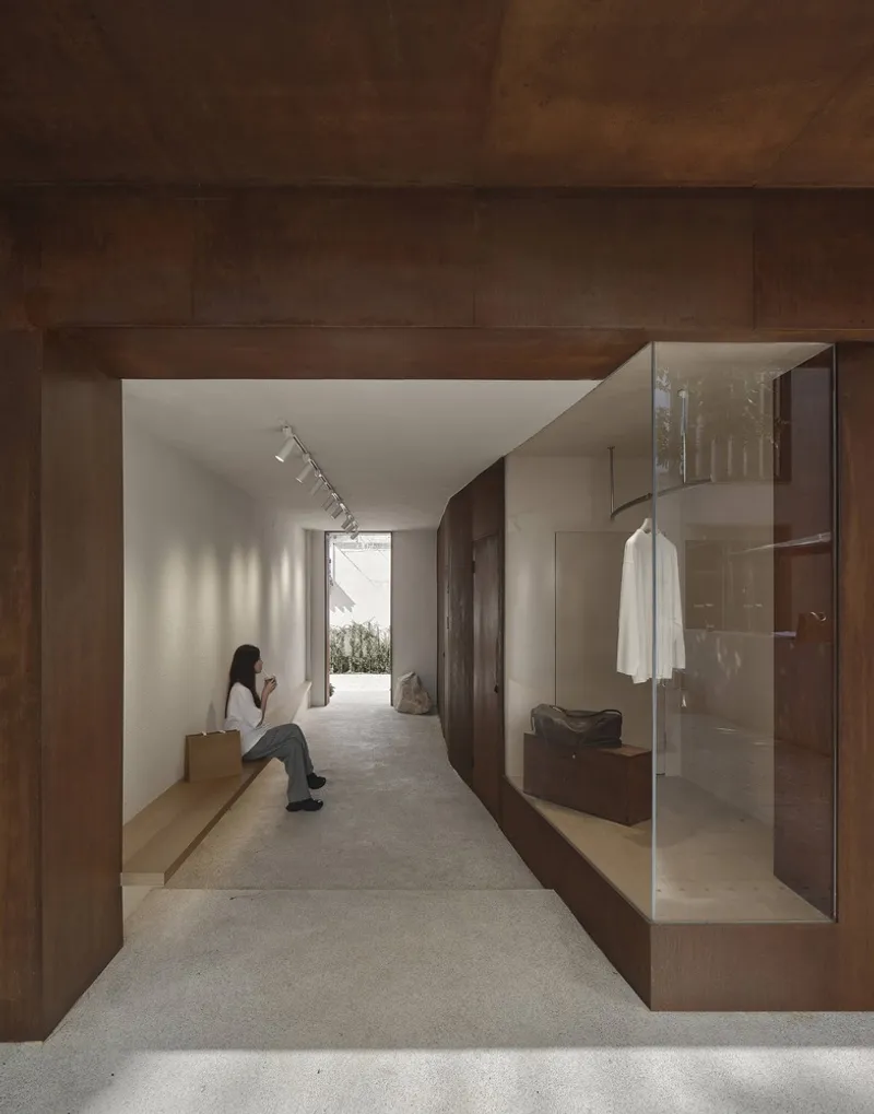 Timber-clad corridor with built-in bench seating and glazed display niche, a visitor seated in afternoon light