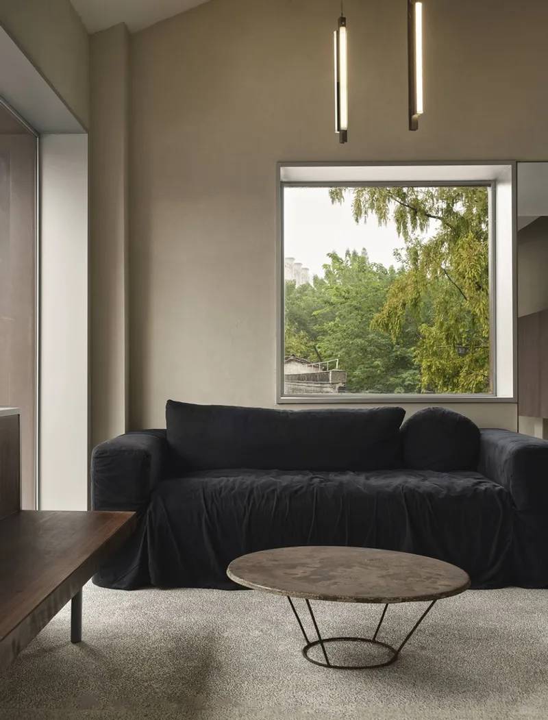 Sitting area with square window framing willow trees and greenery beyond the building