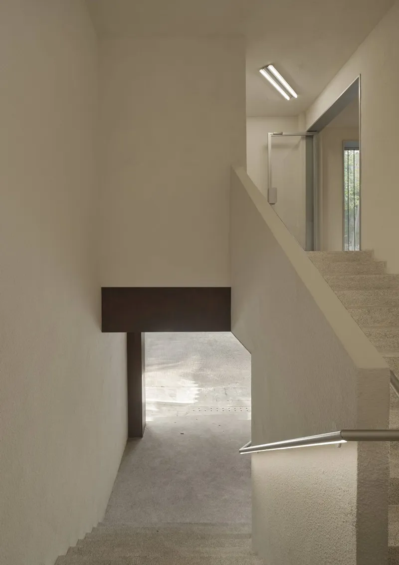 Stairwell with timber beam framing a low passage and daylight filtering through upper skylights