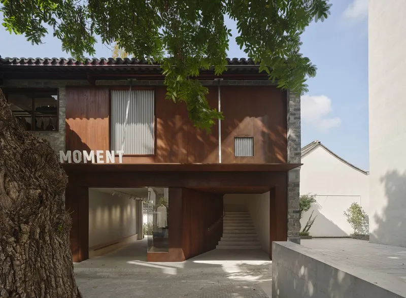 Covered entryway with weathered steel panels and a central staircase beneath an overhanging tree canopy