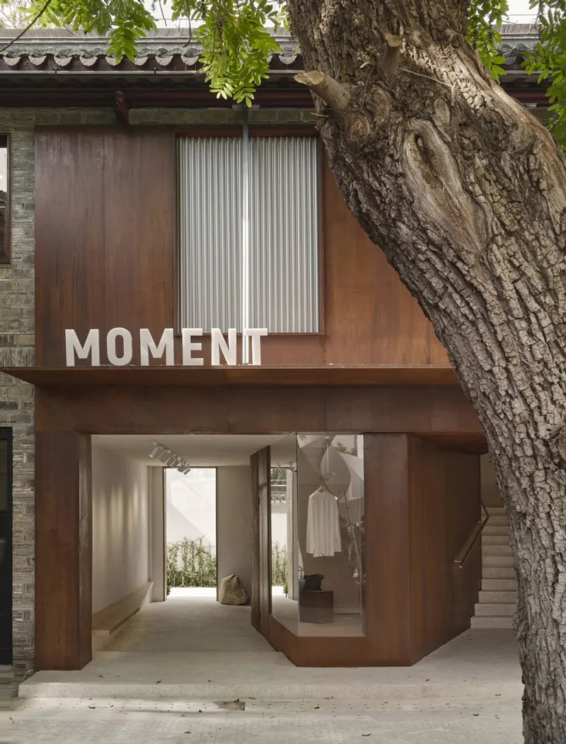 Ground floor passage with weathered steel frames and a glass display box flanked by a tree trunk