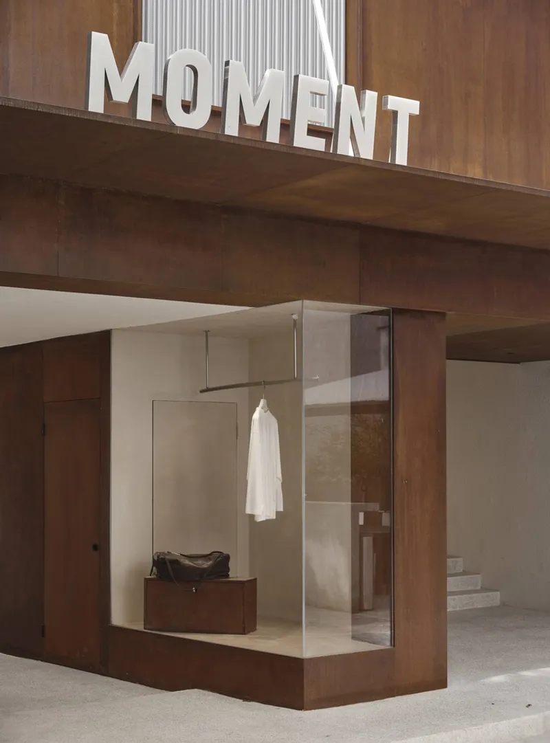 Glass retail display box with hanging garment and leather bench beneath a steel structural overhang