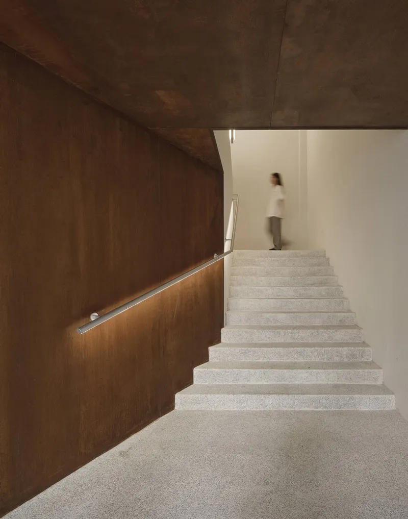 Terrazzo staircase with steel handrail and a figure ascending toward a white upper landing