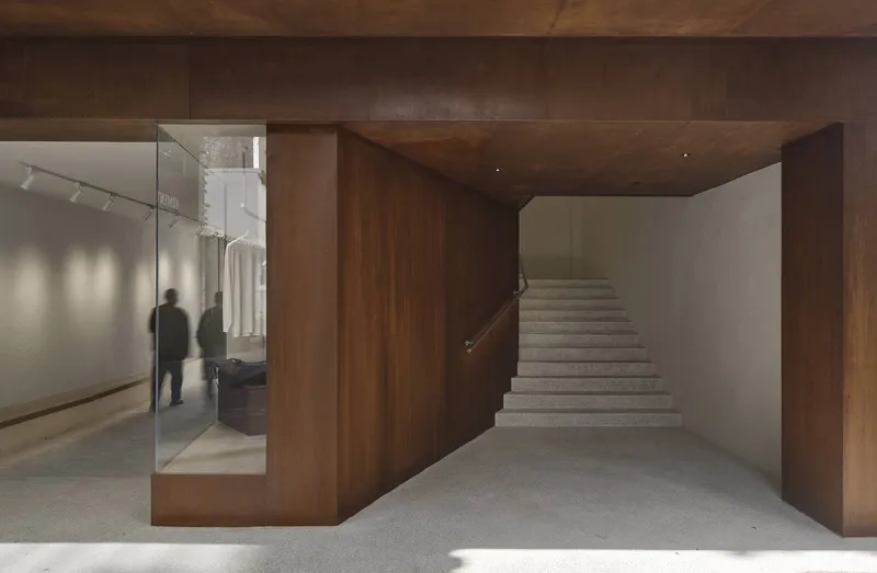 Stone staircase ascending beside dark walnut volume with glass retail partition revealing visitors inside