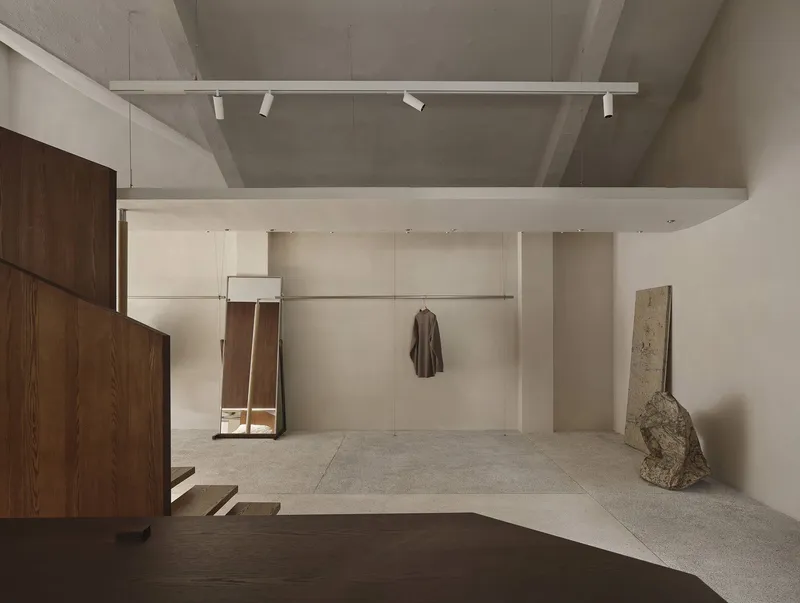 Double-height retail space with exposed concrete beams and single garment suspended from wall-mounted rail
