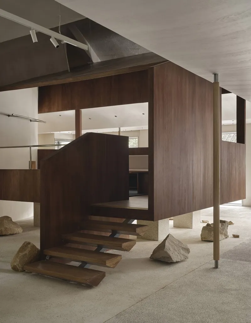 Cantilevered walnut-clad volume with floating treads and large stone boulders on polished terrazzo floor