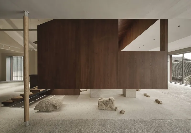Walnut-wrapped sculptural volume with timber column and scattered stones beneath overhanging wooden treads