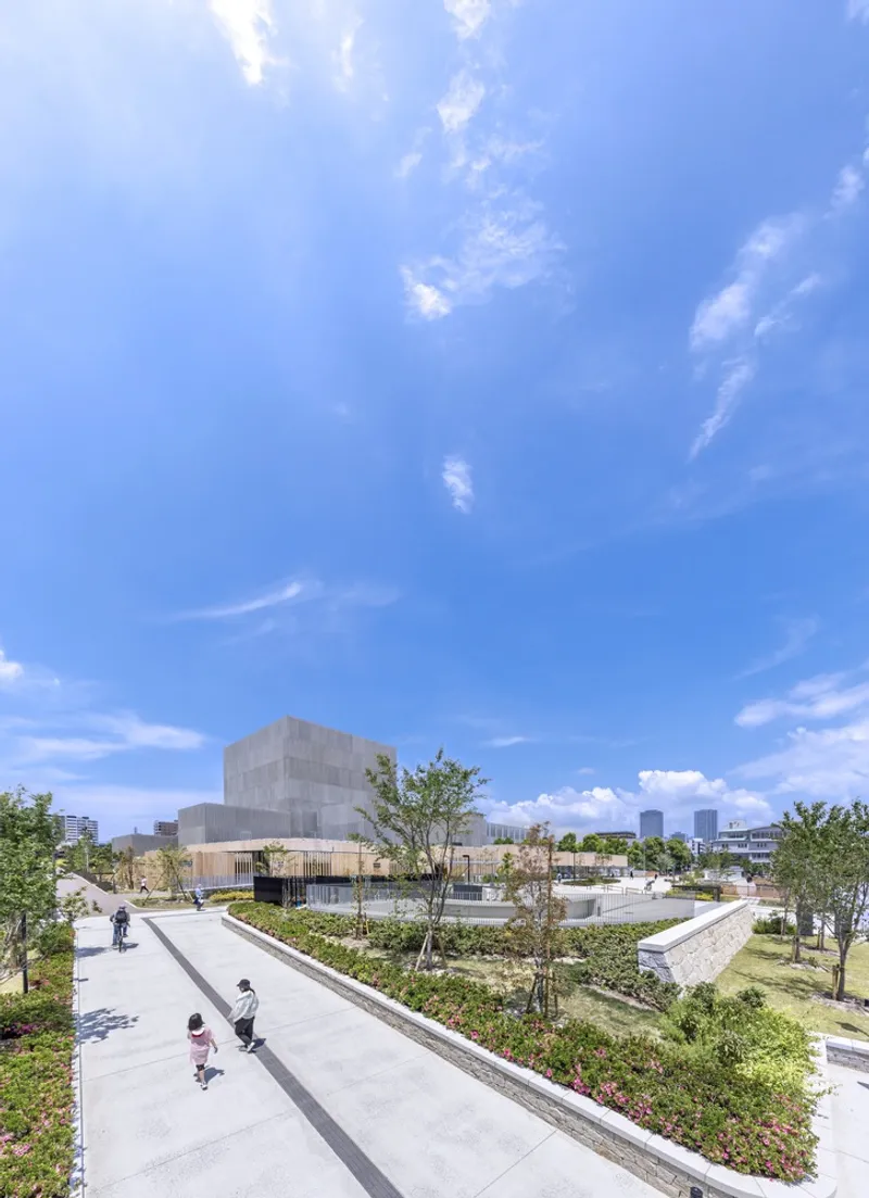 Elevated pathway with pedestrians winding through planted terraces toward the translucent volumes