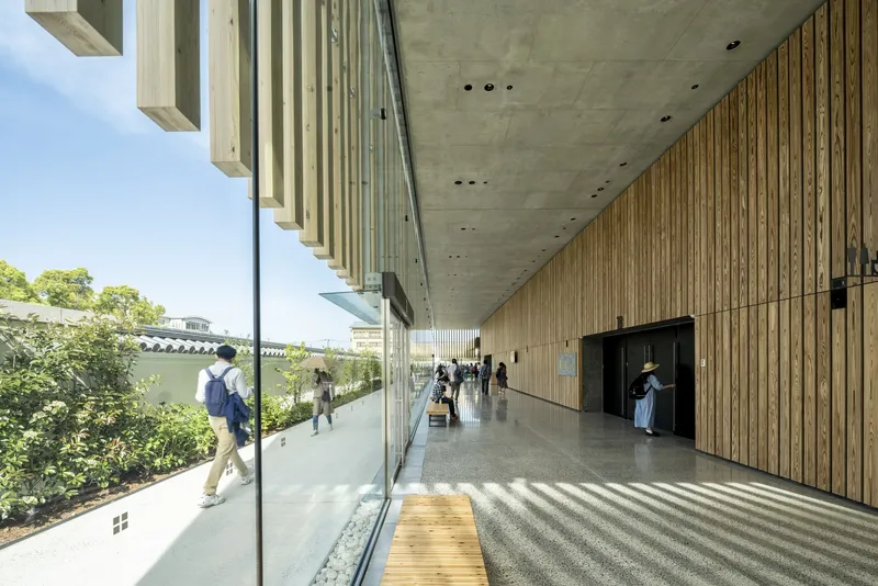 Glass-walled lobby corridor with timber slat wall and concrete ceiling overlooking planted terrace
