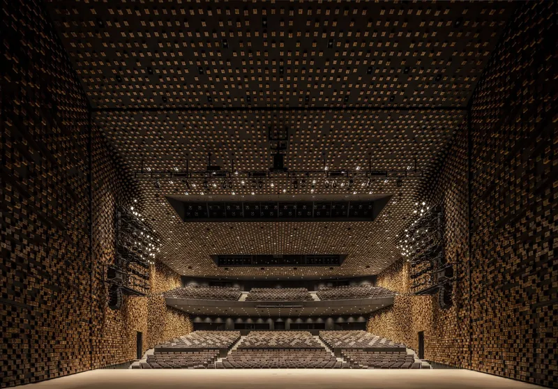 Theatre auditorium with pixelated perforated wood panels wrapping walls and balconies