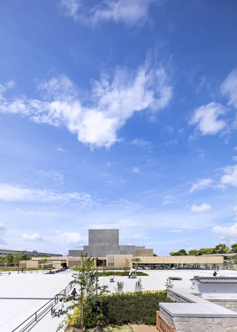 Rooftop view showing a white gravel terrace with planted beds and a ribbed concrete volume under blue sky