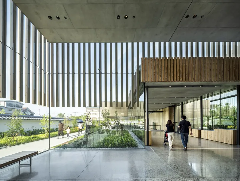Double-height interior lobby with vertical timber screens filtering daylight onto polished terrazzo floors and visitors passing through
