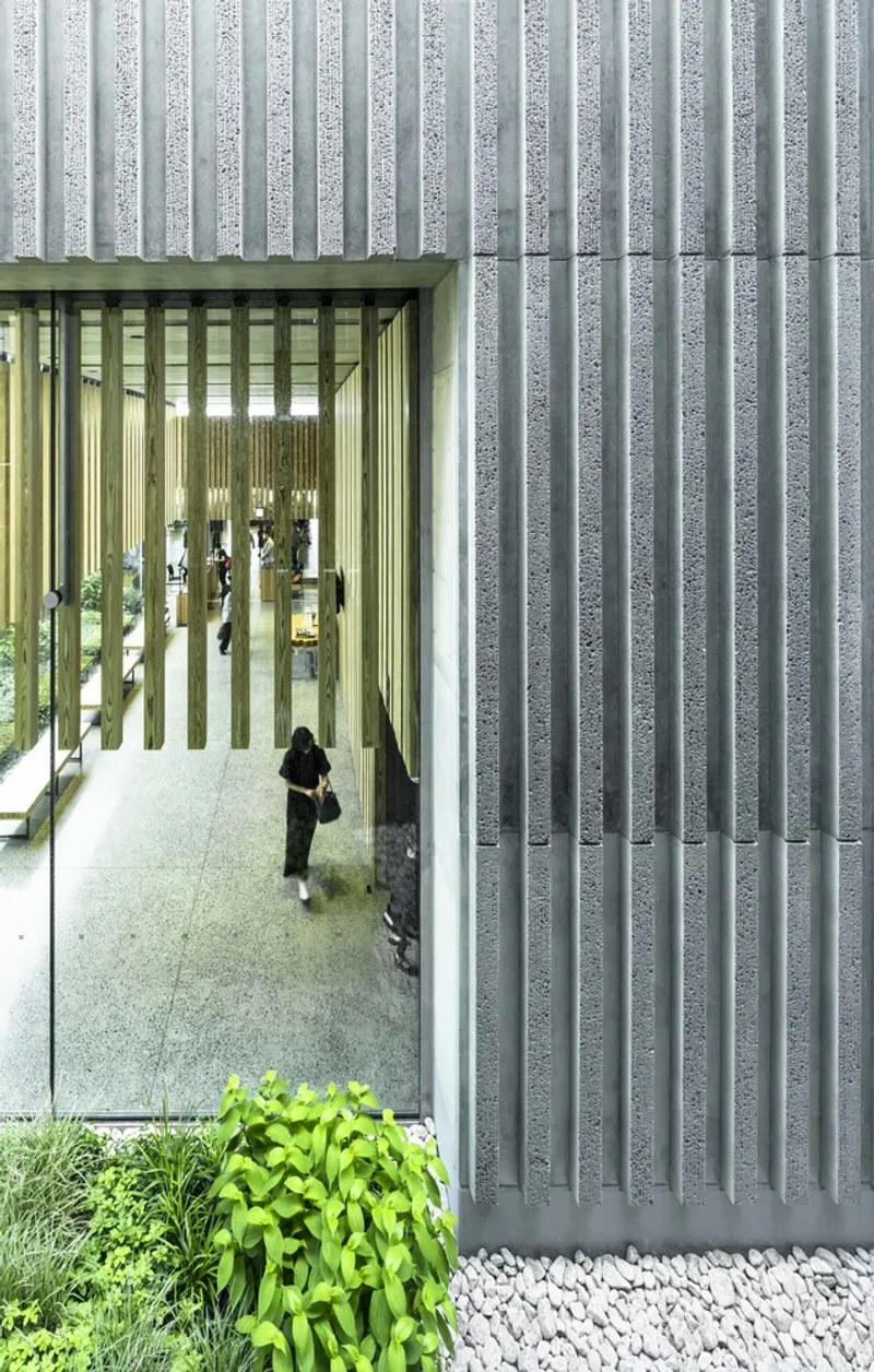 Facade detail showing textured concrete vertical fins with cutout framing an interior corridor and planted edge