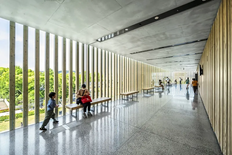 Interior corridor with vertical timber slat screen wall and terrazzo flooring with children playing near benches