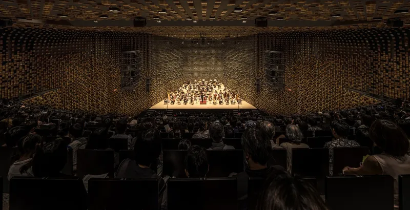 Concert hall interior with pixelated timber block walls and ceiling enclosing the illuminated orchestra stage