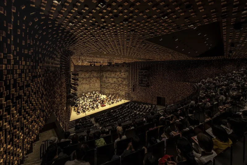 Side balcony view of the auditorium showing textured timber block acoustic surfaces wrapping walls and ceiling