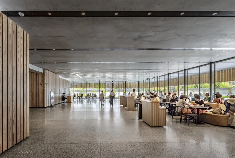 Open common area with terrazzo floors, vertical timber screens, glass partitions, and occupied seating groups