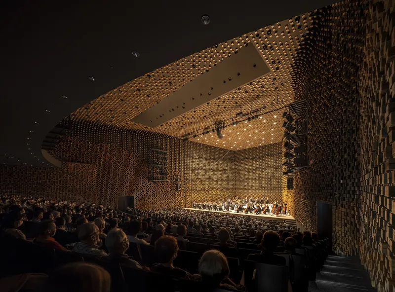 Orchestra performing on stage beneath undulating timber block ceiling and wall surfaces during evening concert