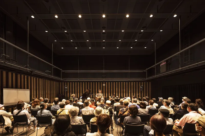 Orchestra rehearsal in a performance hall with coffered dark ceiling and vertical timber acoustic paneling