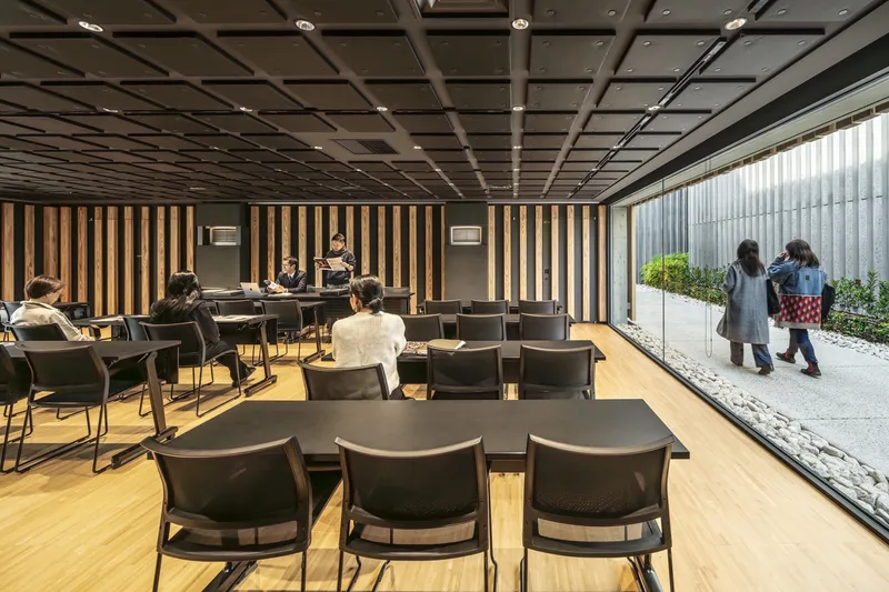 Lobby space with coffered ceiling, vertical timber wall slats and glazed courtyard with pedestrians passing outside