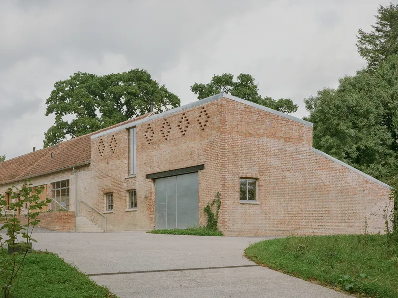 Gabled brick facade with patterned perforations and glazed entrance under an overcast sky