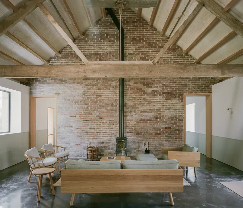 Interior with exposed timber roof trusses and brick gable wall behind wood stove