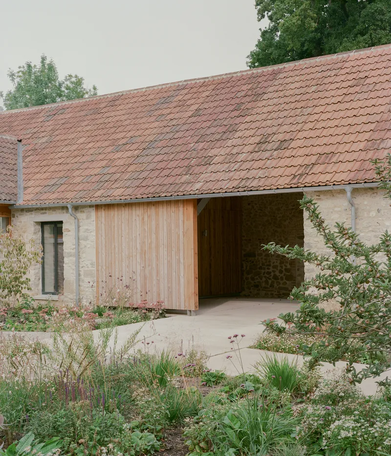 Timber sliding door set within stone walls beneath terracotta tile roof and garden planting