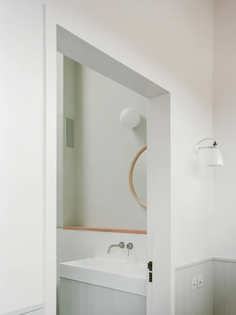 Bathroom vanity with circular mirror framed by recessed white plaster doorway and wall sconce