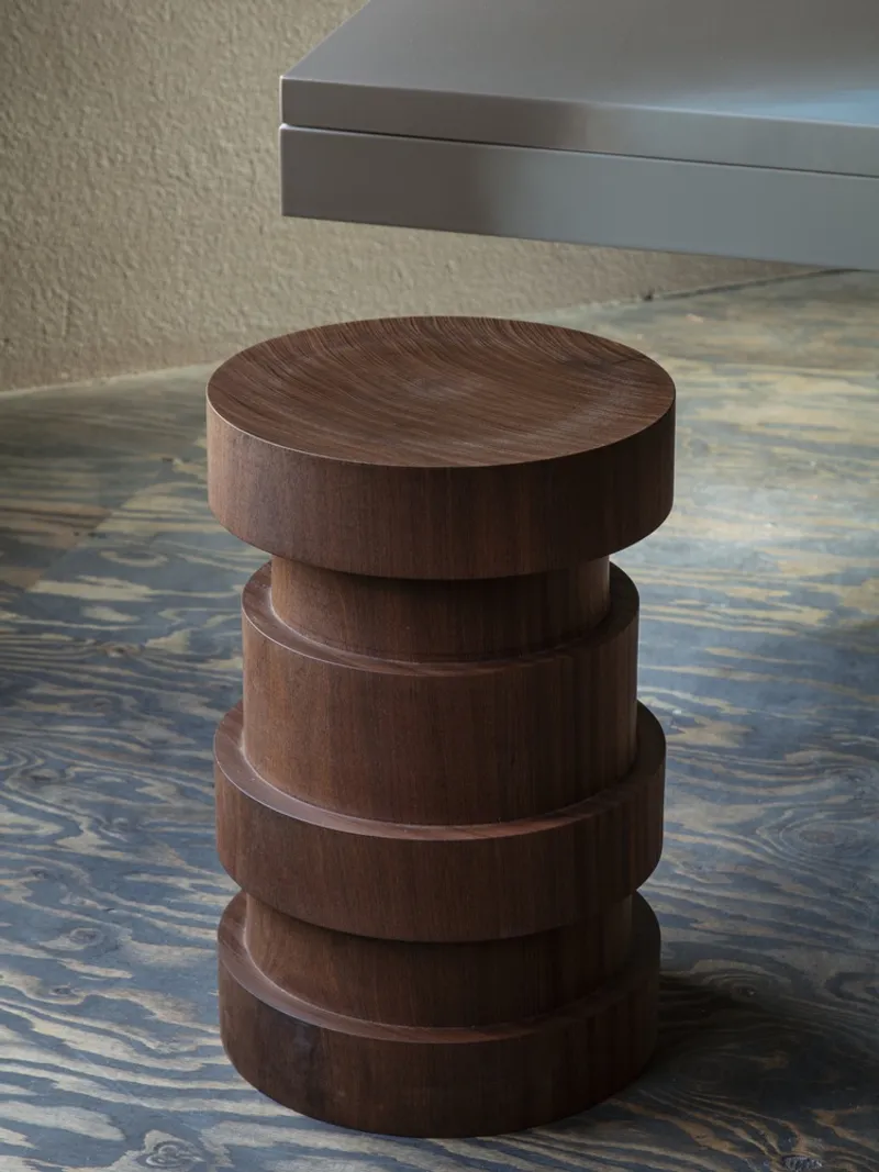 Close-up of a stacked timber stool with four cylindrical sections on patterned wood flooring